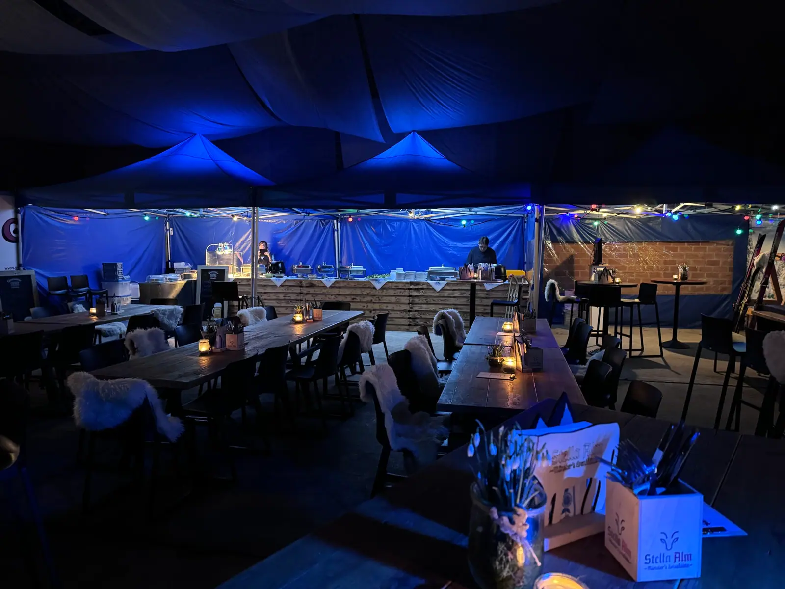 Abendlich beleuchtetes Eventzelt mit Tischen und Buffet