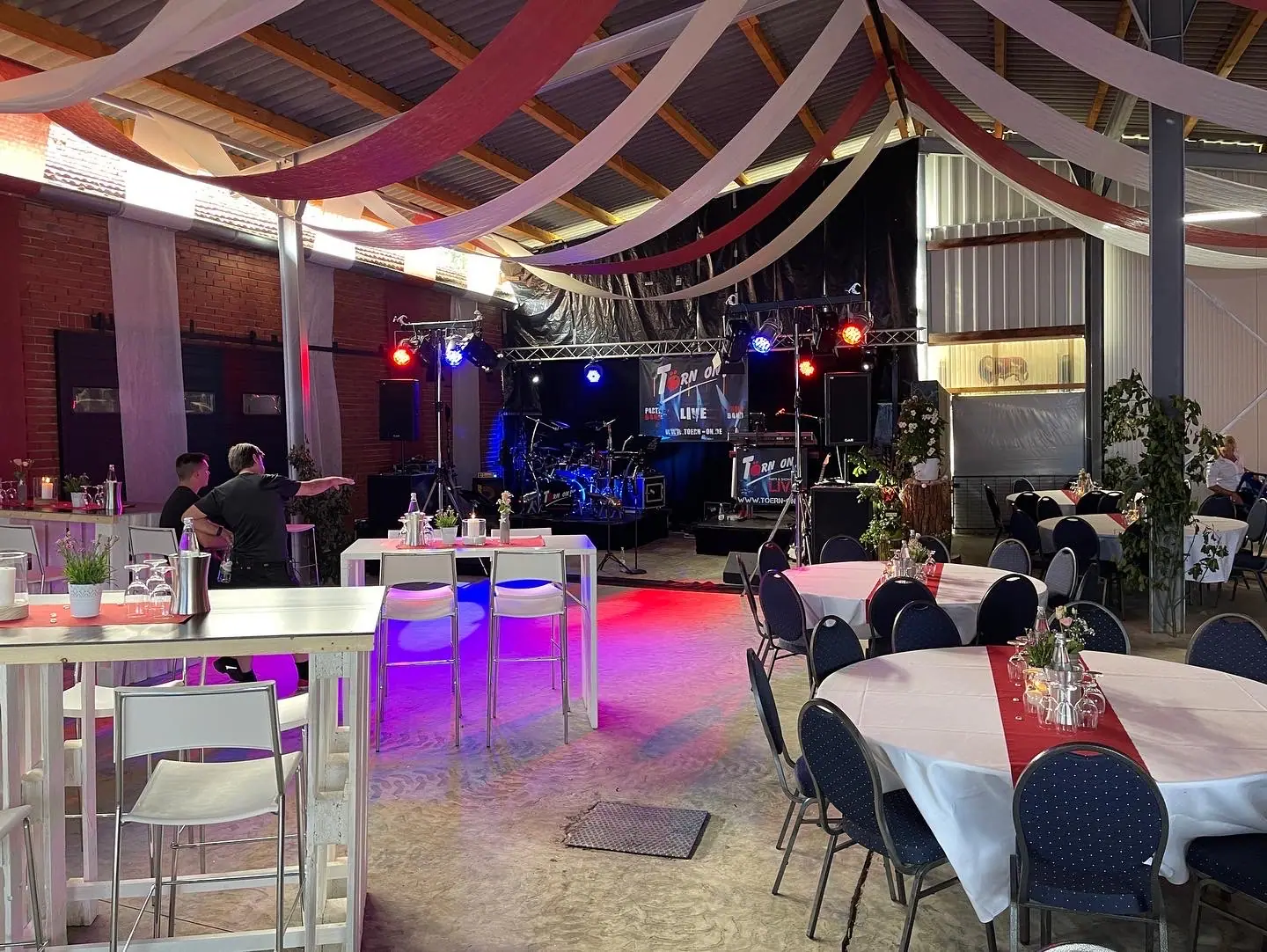 Dekorierte Eventhalle mit Bühne, Lichtern und eingedeckten Tischen
