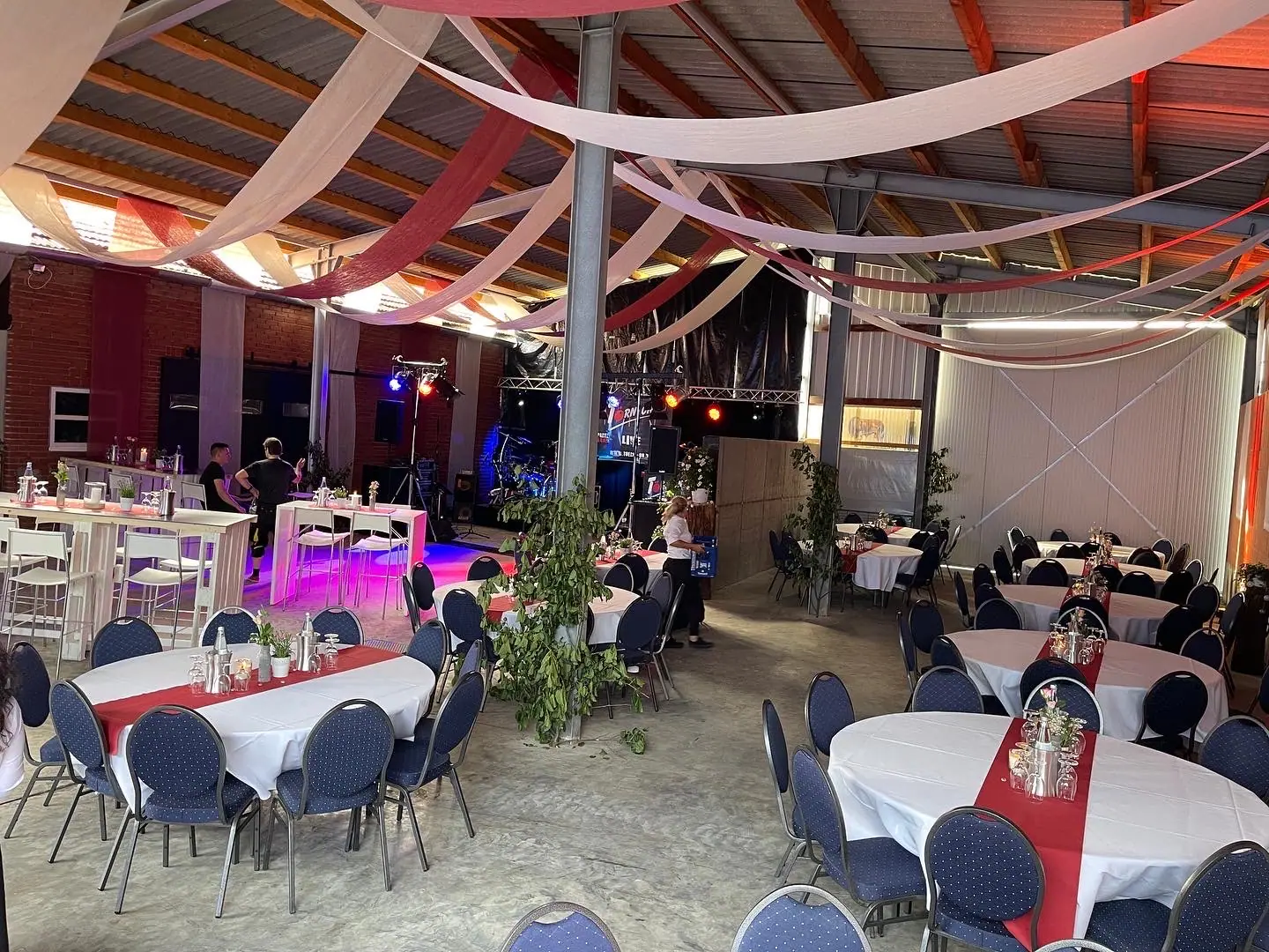 Festlich eingedeckte Halle mit runden Tischen, Stuhlhussen und Tischläufern