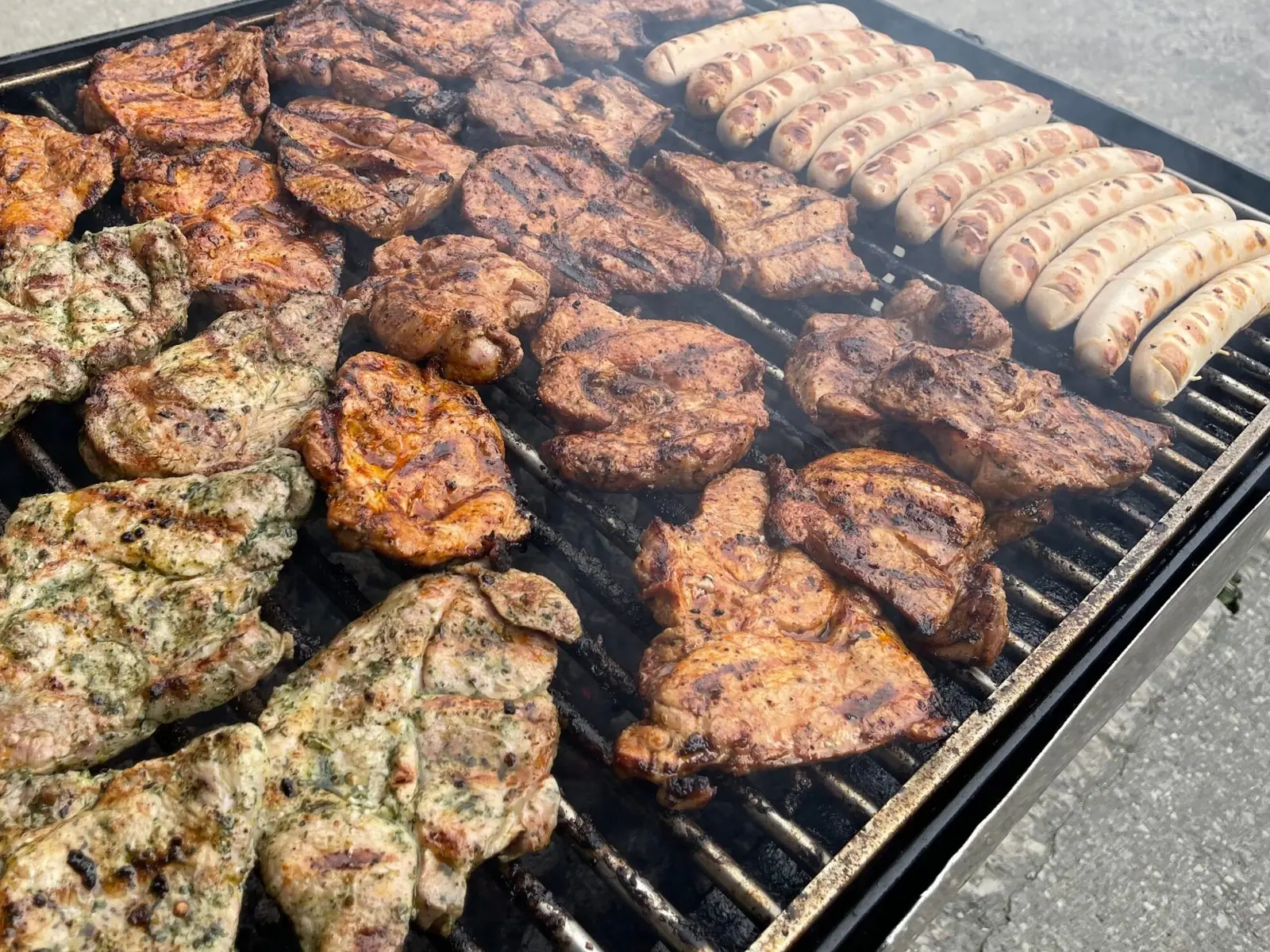 Grillrost mit eingelegten Steaks und Bratwürsten bei einem Grillbuffet