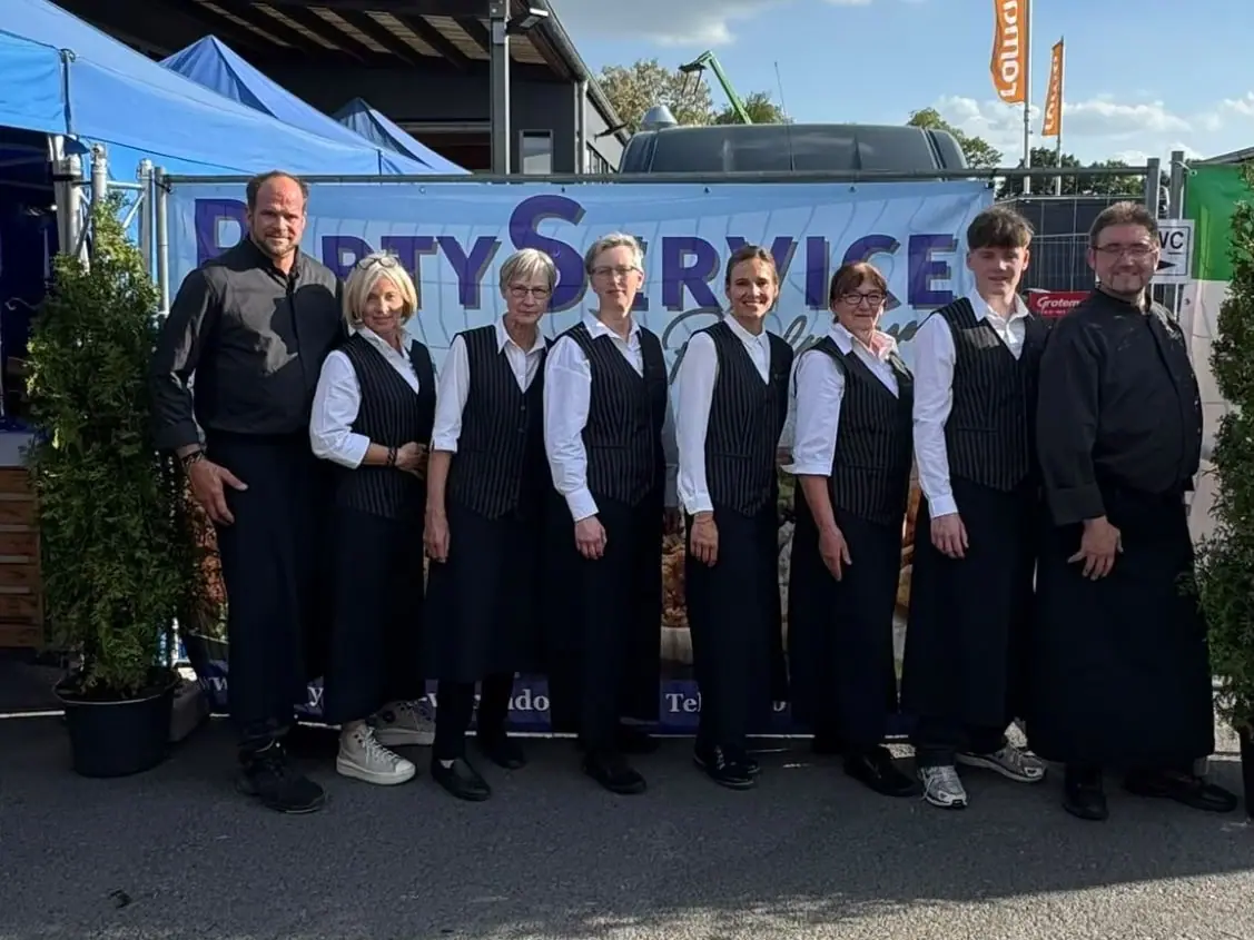 Das Team von Partyservice Pöppelmann – Servicekräfte und Köche vor dem PartyService-Banner